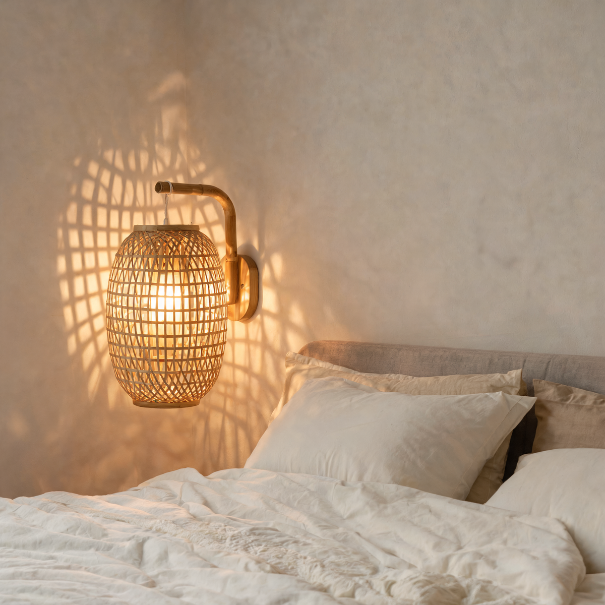 Hand-woven bamboo lantern wall sconce lit beside a bed
