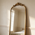 Gold arched vintage mirror against pale plaster in a period bedroom